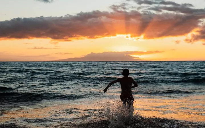 Junge rennt ins Meer beim Sonnenuntergang