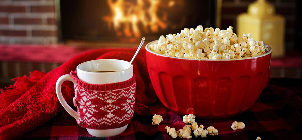 Tasse Tee mit Popcorn vor Kamin