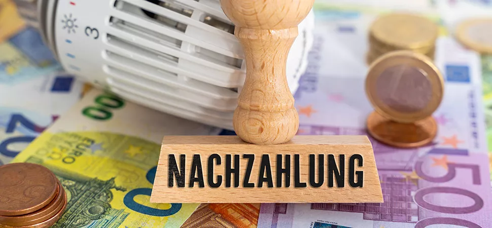 Nachzahlung Nebenkosten Geldscheine übereinander, darauf ein Heizungsthermostat und ein Stempel mit der Aufschrift "Nachzahlung"