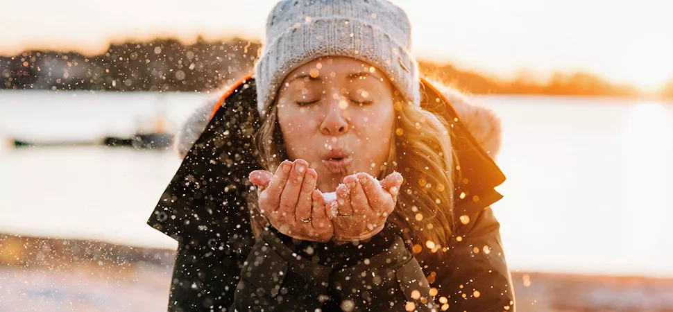 Frau im Winter mit Schnee Eine Frau in Winterjacke & Mütze pustet Schnee in die Kamera