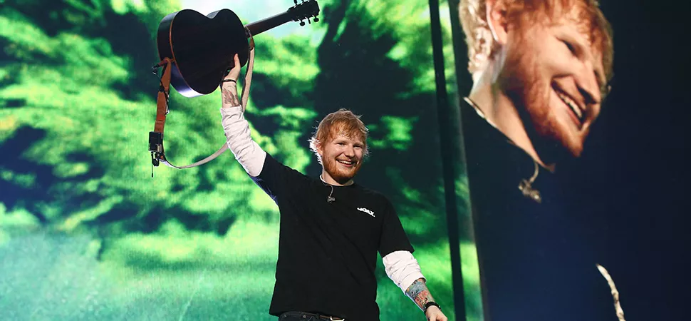 Ed Sheeran bei einem Auftritt Ed Sheeran hält eine Gitarre in die Luft und freut sich.