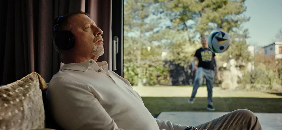 Boris Becker sitzt entspannt auf dem Sofa während Stefan Effenberg im Garten Fußball spielt