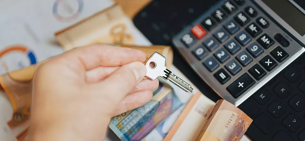 Eine Person legt Geld vor einen Taschenrechner und hat einen Hausschlüssel in der Hand