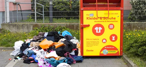 Altkleidercontainer mit einem Haufen Müll nebendran