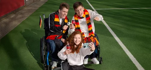 Drei Teenager in Deutschland-Fanoutfits und mit einer Coca Cola in der Hand machen ein Selfie