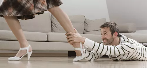 Ein Mann hält sich am Bein einer Frau fest, die weggehen möchte.