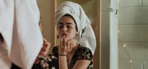 Frau mit Handtuchturban schaut sich im Spiegel an