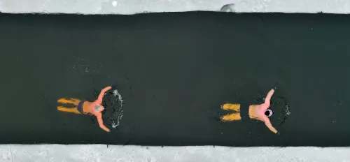Zwei Personen schwimmen im Wasser mit Eis umgeben