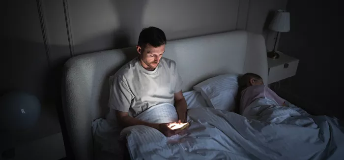 Ein Mann liegt im Bett und scrollt auf seinem Handy.