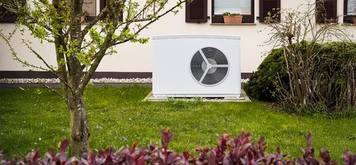 Eine Wärmepumpe steht vor einem Einfamilienhaus im Garten.