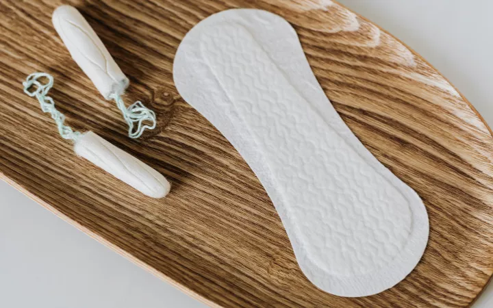 Tampons und Binde Zwei Tampons und eine Binde auf einem Holzbrett