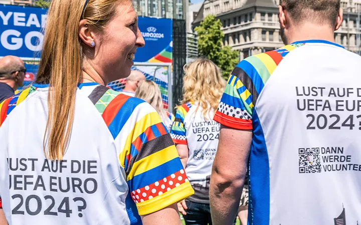 UEFA EURO 2024 - Werde Volunteer! Eine Frau und ein Mann tragen Shirts auf deren Rücken "Lust auf die UEFA EURO 2024?" steht