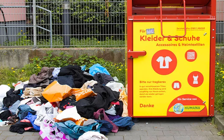 Altkleidercontainer mit einem Haufen Müll nebendran