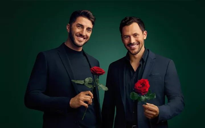 Die Bachelors 2024 Die beiden Bachelors 2024 Dennis und Sebastian stehen im schwarzen Anzug nebeneinander und halten jeweils eine Rose in der Hand.