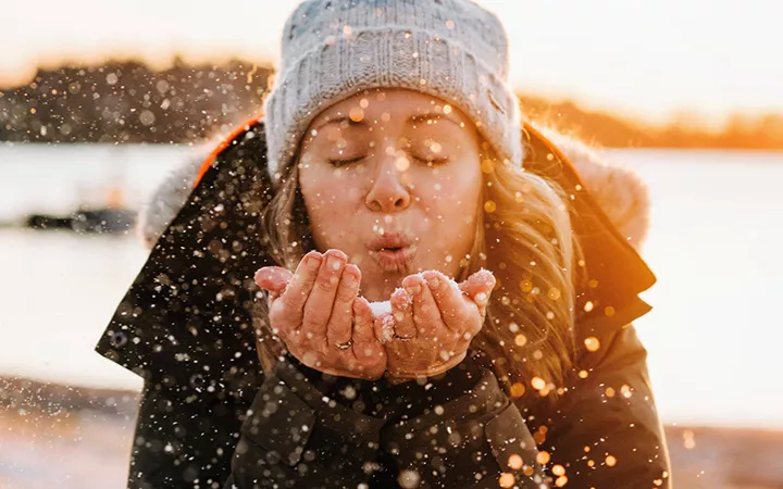 Frau im Winter mit Schnee Eine Frau in Winterjacke & Mütze pustet Schnee in die Kamera