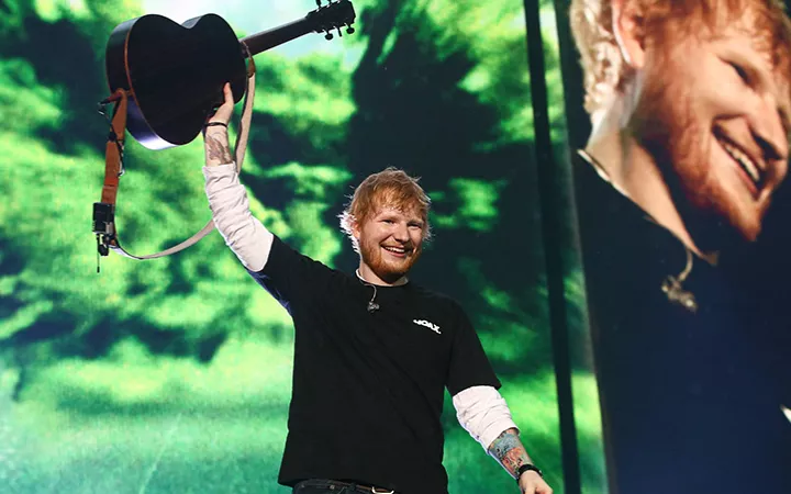 Ed Sheeran bei einem Auftritt Ed Sheeran hält eine Gitarre in die Luft und freut sich.