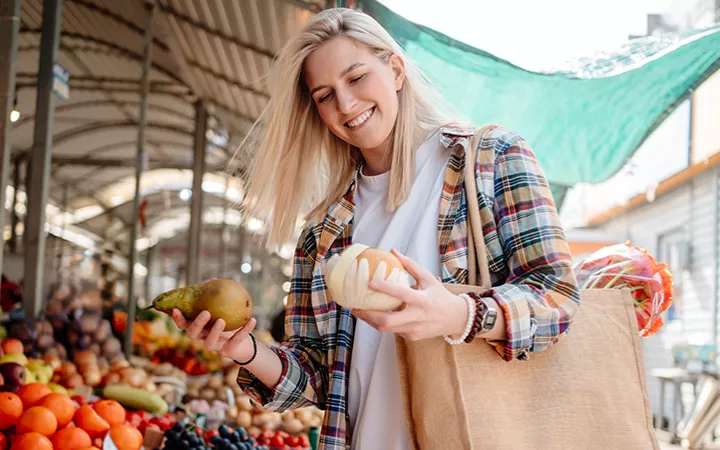 Frau auf dem Wochenmarkt Frau auf dem Wochenmarkt hält zwei Früchte in der Hand
