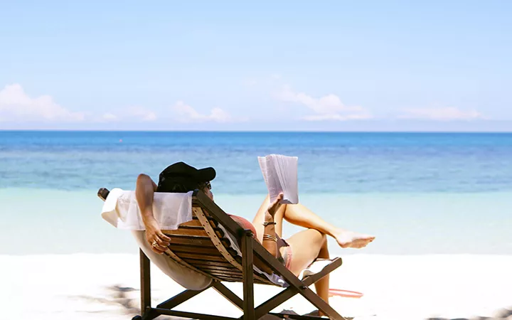 Frau am Strand Frau liegt auf einem Liegestuhl mit Meerblick und liest ein Buch