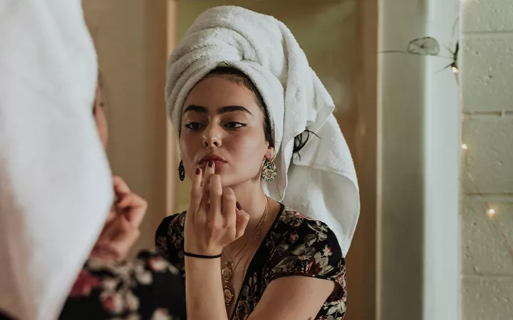 Frau mit Handtuchturban schaut sich im Spiegel an