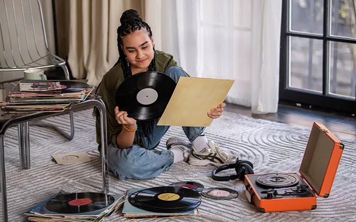 Ein Mädchen sitzt auf dem Boden und schaut sich eine Vinylplatte an.