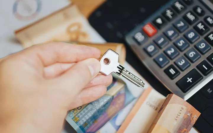 Eine Person legt Geld vor einen Taschenrechner und hat einen Hausschlüssel in der Hand