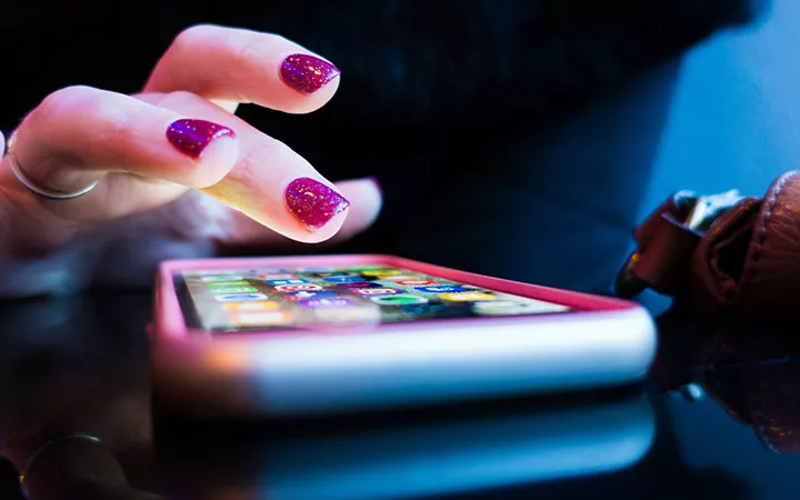 Hand mit pinken Nägeln tippt auf ein Smartphone
