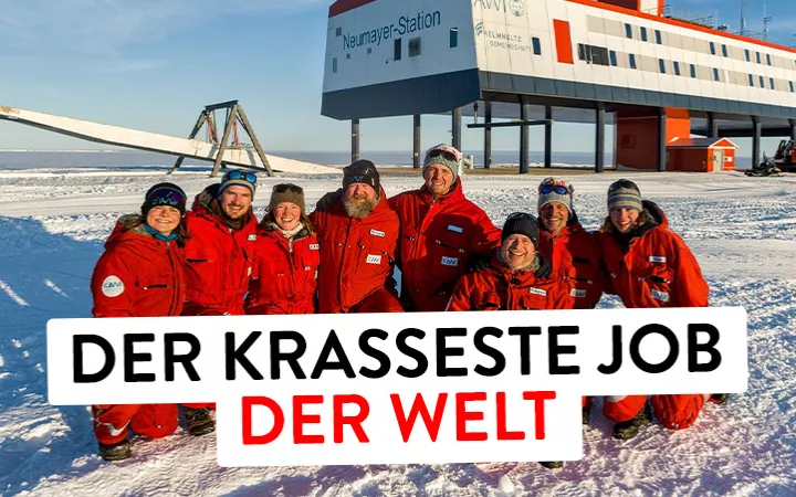 Auf dem Bild sind 8 Menschen in roten Schneeanzügen zu sehen. Sie bilden das überwinterungsteam auf der deutschen Froschungsstation Neumeyer 3 in der Antarktis. Unter ihnen ist Eisund im Hintergrund sieht man die Station.