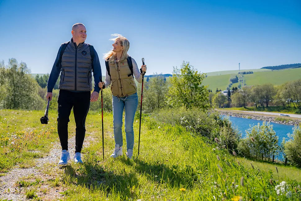 Zwei Wanderer mit Stöcken auf einer Wiese neben einem Fluss