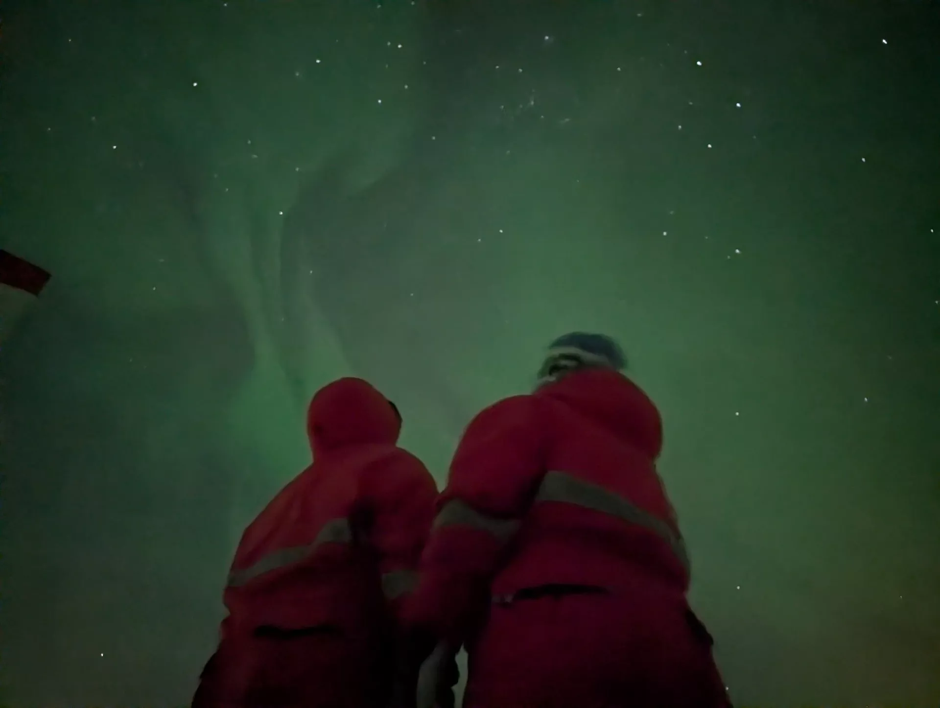 Zwei Forschende in roten Schneeanzügen in der Antarktis unter grünen Polarlichtern