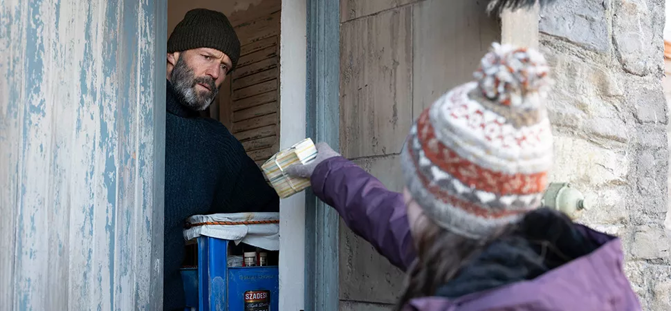 Ein Mann öffnet eine Tür und bekommt was gereicht von einer Person