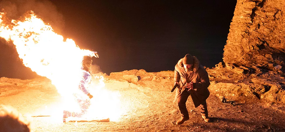 Eine brennende Person, daneben rennt eine andere Person weg