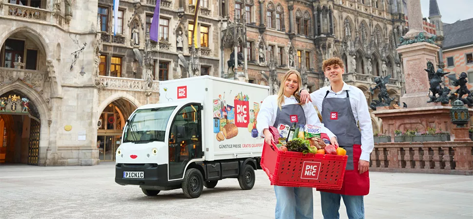 Eine Frau und ein Mann mit Lebensmittelkörben vor einem kleinen Lieferauto in München
