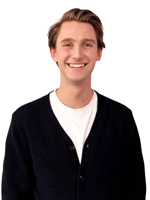 Junger blonder Mann mit weißem Shirt und schwarzem Cardigan lächelt in die Kamera