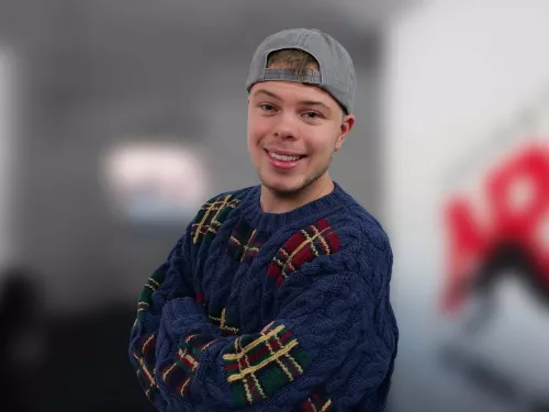 Junger Mann in einem gemustertem blauen Pullover und grauer Kappe