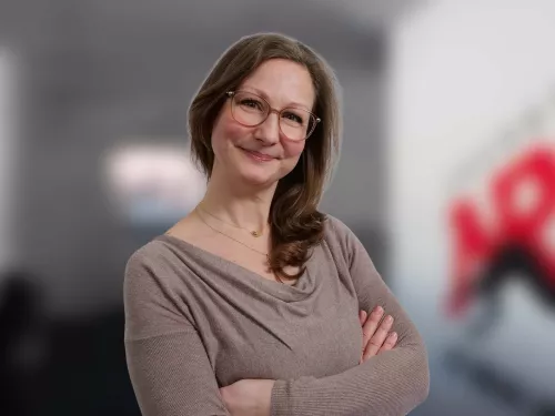 Frau mit braunen Haaren in einem sandfarbenen Oberteil